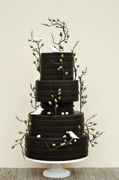 a three tiered cake with white flowers and birds on the top is sitting on a pedestal