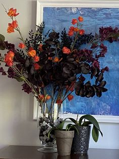 two vases filled with flowers sitting on top of a wooden table next to a painting