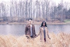 two people are standing in tall grass by the water holding hands and looking off into the distance