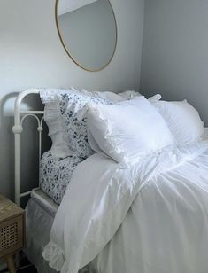 a bed with white linens and pillows in a bedroom next to a round mirror