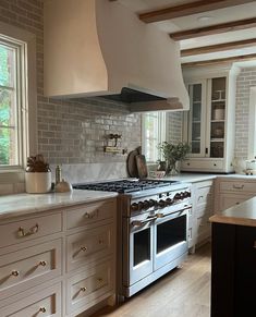 a kitchen with an oven, stove and counter tops in white painted wooden cabinets next to a window