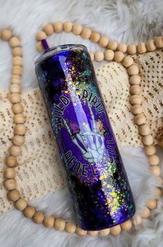 a purple tumbler sitting on top of a white rug next to beads and a wooden bead necklace