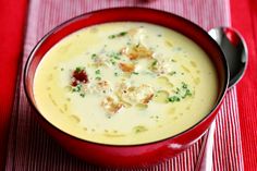 a red bowl filled with soup sitting on top of a striped table cloth next to a spoon