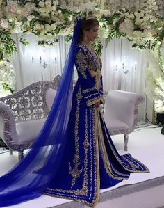 a woman in a blue and gold bridal gown standing next to a white couch