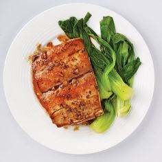 a white plate topped with meat and greens on top of a table next to a fork