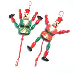 two red and green ornaments are hanging from strings on a white surface, one is holding the other's hand