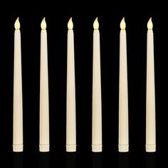 six candles lined up in a row on a black background with one candle lit and the other turned down