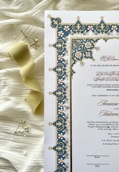 an ornate wedding card with gold and blue trimmings on a white bed sheet