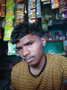 a man in striped shirt looking at camera with food on display behind him and shelves full of snacks