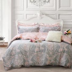 a white bed with pink and blue comforter in a room next to a chandelier