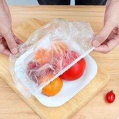 the person is packing up their tomatoes and oranges in a plastic bag on top of a cutting board