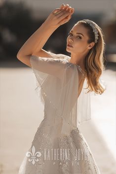 a woman in a white dress posing for the camera with her hand on her head