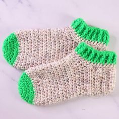 two crocheted green and white socks on a marble surface