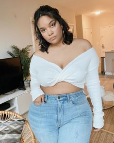 a woman standing in front of a tv wearing high waist jeans and a white crop top