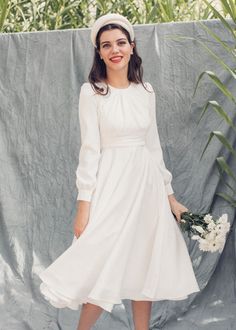 a woman in a white dress and hat is posing for the camera with her hands on her hips