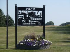 a sign for kolon farms in the middle of a field with flowers and trees