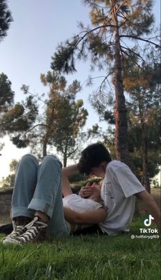 a man sitting in the grass with his hands on his face next to a tree