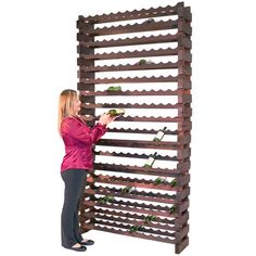 a woman standing next to a tall wooden wine rack filled with lots of green plants