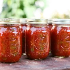 four jars filled with red sauce sitting on top of a wooden table