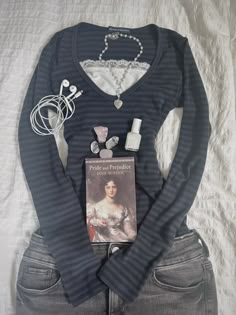 a woman's shirt and necklace laying on top of a white sheet with a book