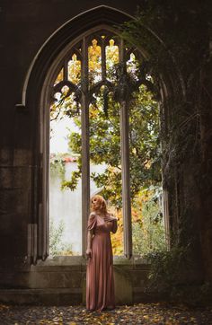 a woman standing in front of an arched window with leaves on the ground around her