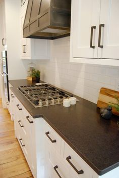 a stove top oven sitting inside of a kitchen next to white cabinets and wooden floors