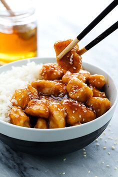 a white bowl filled with rice and chicken on top of a table next to chopsticks