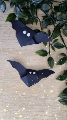 two paper bats with faces on them are sitting next to some green leaves and branches