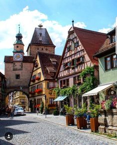 a cobblestone street lined with tall buildings and flowers in front of a clock tower