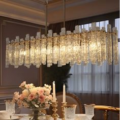 a chandelier hanging over a dining room table with flowers and candles on it