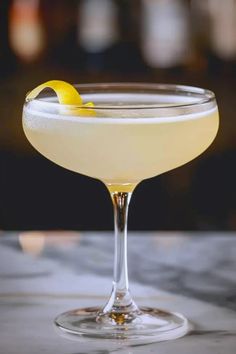 a close up of a drink in a glass with a lemon on the rim and garnish