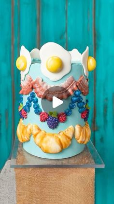 a blue cake with an egg on top and fruit around the edges, sitting on a wooden block