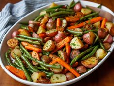 a white bowl filled with potatoes, green beans and carrots on top of a wooden table