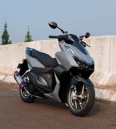 the motorcycle is parked on the side of the road next to a concrete wall and trees