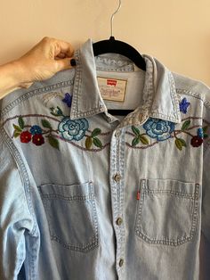 a woman's hand holding onto a blue jean shirt with flowers on the front