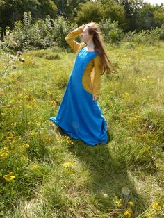 a girl in a blue and yellow dress is standing in the grass with her hands on her head