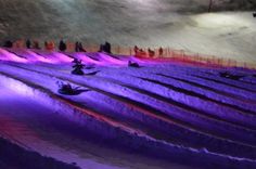 people are skiing down a snowy hill at night with colored lights on the snow and trees in the background