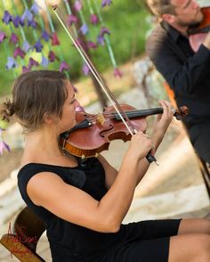 a woman playing the violin in front of other people sitting down and looking at her