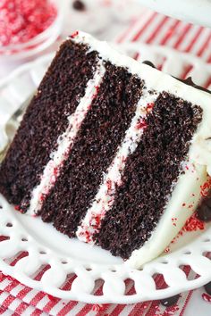 a slice of chocolate cake with white frosting and red sprinkles on a plate