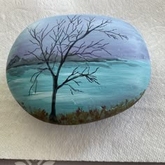 a painted rock sitting on top of a white cloth covered floor next to a tree