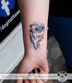 an owl tattoo is on the wrist of a woman's left hand and it has blue ink