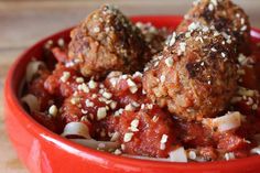 some meatballs are in a red bowl on a wooden table with onions and seasoning