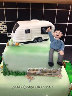 a birthday cake with a man sitting on top of it and a camper in the background