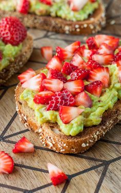 two pieces of bread with strawberries and guacamole on top, sitting on a cutting board