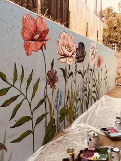 some paint cans are sitting on the ground next to a wall with flowers painted on it