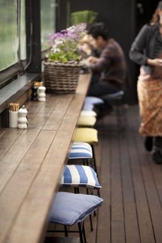 two people sitting at a long wooden table with blue and white striped cushions on it