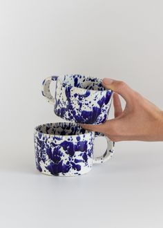 two blue and white coffee cups being held by a person's hand on a white background