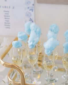 champagne glasses filled with blue and white flowers on a tray in front of a table