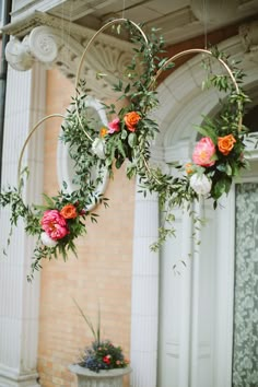 two hoop hanging from the ceiling with flowers and greenery on it in front of a building