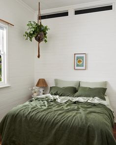 a bed with green sheets and pillows next to a window in a room that has white walls